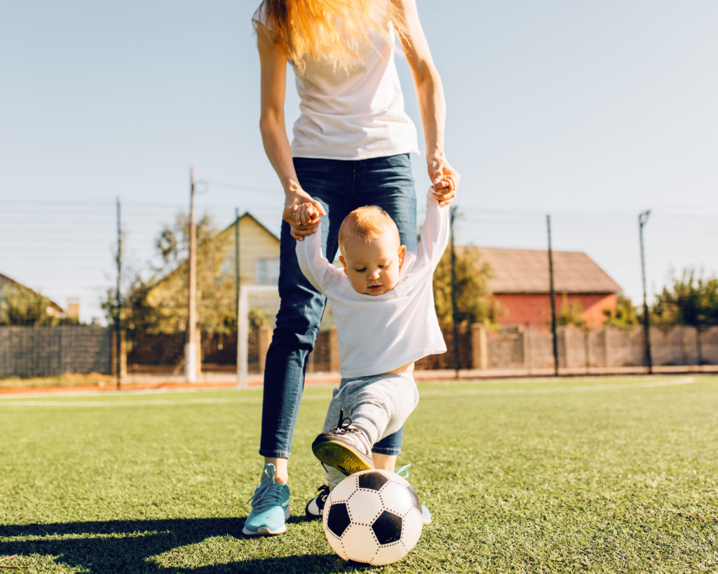 Summer nanny playing soccer with a baby in a fun, outdoor activity, showcasing the nanny's engagement and creativity in child care during the summer nanny job