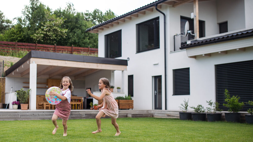 What High-Net-Worth Families Want in a Nanny. Two small girls sisters playing with a ball outdoors in the backyard, running.